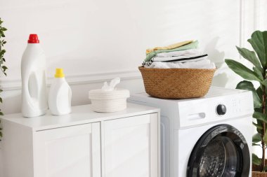 Çamaşır makinesinde temiz giysiler ve kapalı alanda deterjan olan çamaşır sepeti.