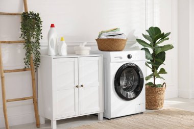 Çamaşır makinesinde temiz giysiler ve kapalı alanda deterjan olan çamaşır sepeti.