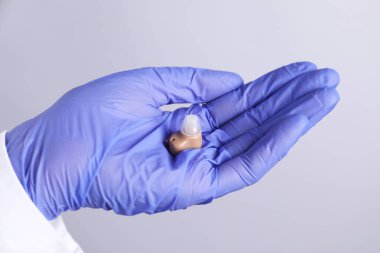 Açık gri arkaplanda işitme cihazı olan doktor, yakın plan.