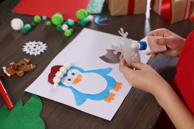 Küçük çocuk Noel kartpostalı hazırlıyor, ahşap masada, yakın plan. Çocuk el yapımı.