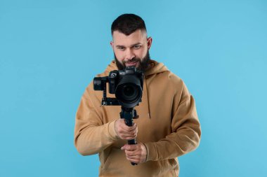 Açık mavi arkaplanda kameralı titreşim dengeleyici kullanan kameraman