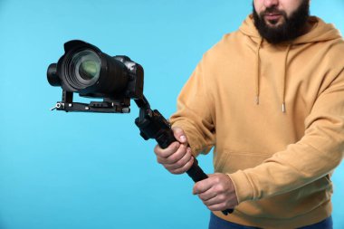 Açık mavi arkaplanda kamerası olan titreşimli dengeleyici kullanan kameraman, kapat