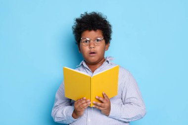 Açık mavi arkaplan üzerine kitabı olan şirin bir çocuk.