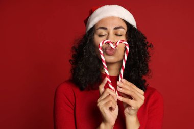 Kırmızı arka planda Noel Baba şapkası ve şeker kamışı olan güzel bir kadın. Noel sezonu