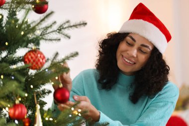 Noel Baba şapkalı güzel bir kadın Noel ağacını evde süslüyor.