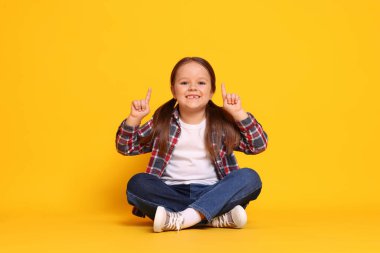 Tatlı küçük kız turuncu arka plandaki bir şeyi işaret ediyor.