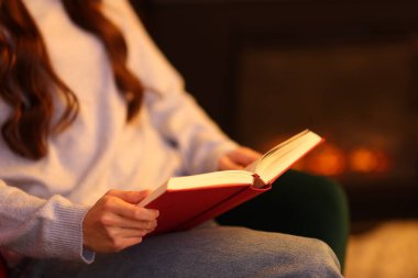 Evdeki şöminenin yanında kitap okuyan kadın, yakın çekim.