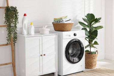 Çamaşır makinesinde temiz giysiler ve kapalı alanda deterjan olan çamaşır sepeti.