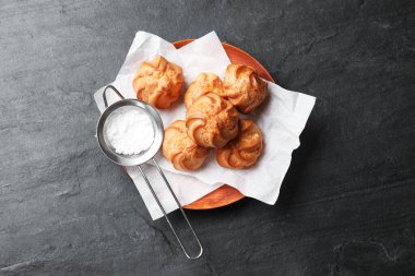 Lezzetli profiteroller ve siyah masaya pudra şekerli süzgeç.