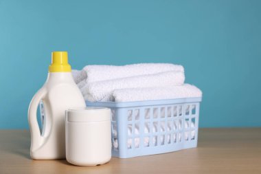 Temiz havlular ve ahşap masa üzerinde deterjan dolu çamaşır sepeti açık mavi arkaplan, metin için boşluk