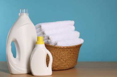 Temiz havlular ve ahşap masa üzerinde deterjan dolu çamaşır sepeti açık mavi arkaplan, metin için boşluk