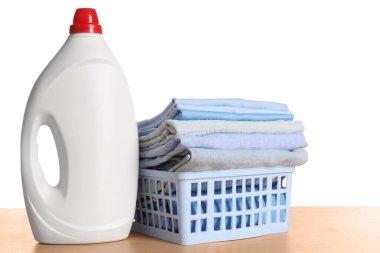 Temiz elbiseli çamaşır sepeti ve ahşap masada beyaz arka planda deterjan.