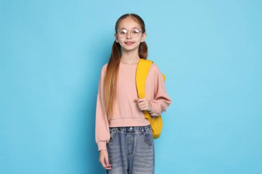 Açık mavi arka planda sırt çantası olan sevimli bir kız.