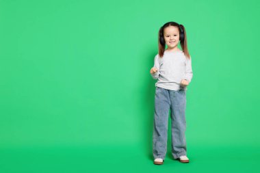 Yeşil arka planda kulaklıklar takan tatlı küçük kız, mesaj atmak için yer var.