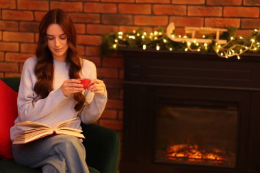 Evde şöminenin yanında kahve kitabı okuyan bir kadın, mesaj atmak için yer var.