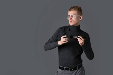 Gri arka planda toz ve fırçayla makyaj sanatçısı. Metin için boşluk