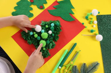 Küçük çocuk sarı masada Noel kartpostalı hazırlıyor. Çocuk el yapımı.