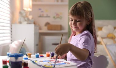 Beyaz masa içinde fırça çizen küçük kız.