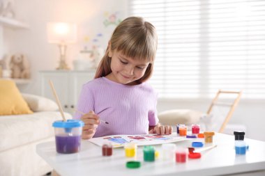 Beyaz masa içinde fırça çizen küçük kız.