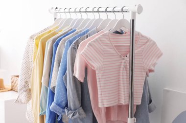 Beyaz duvarın yanında askıda asılı farklı şık kıyafetler, yakın plan.