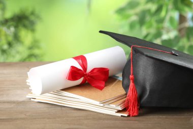 Mezuniyet şapkası, diploma ve defterler ahşap masanın üzerinde bulanık arka plan, yakın plan