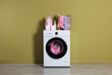 Modern çamaşır makinesi, deterjan ve zeytin duvarının yanındaki kıyafetler.