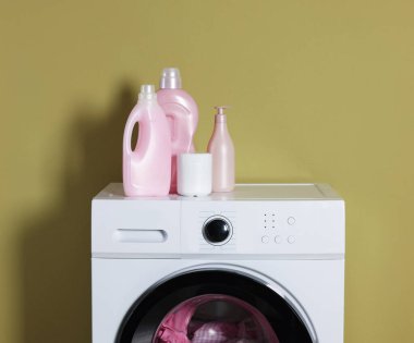 Modern çamaşır makinesi, deterjan ve zeytin duvarının yanındaki kıyafetler.