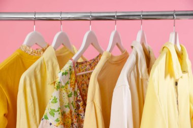 Pembe arka planda askıda asılı farklı şık kıyafetler, yakın plan.