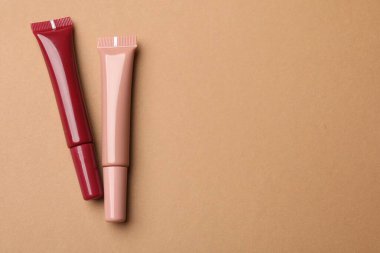 Kahverengi arka planda farklı dudak parlatıcıları, düz yatış. Metin için boşluk