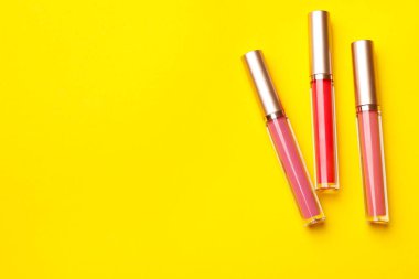 Sarı arka planda farklı dudak parlatıcıları, düz yatış. Metin için boşluk