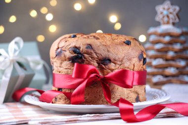 Masada kırmızı kurdeleyle süslenmiş, bulanık ışıklara karşı nefis bir Noel pastası, yakın plan. Bokeh etkisi