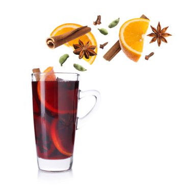 Sıcak şarap. Baharatlar ve portakal dilimleri beyaz arka planda cam bardak sıcak içeceğe dökülüyor.