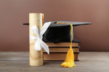 Mezuniyet şapkası, diploma ve kitaplar ahşap masa üzerinde kahverengi arka plan, yakın plan