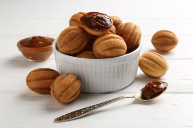 Lezzetli fındık şekilli kurabiyeler haşlanmış süt ve kaşık beyaz ahşap masada, yakın plan.