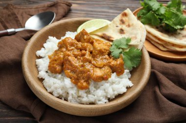 Pirinçli tavuk tikka masala, kişniş, kireç ve lavaş ahşap masada, yakın plan.
