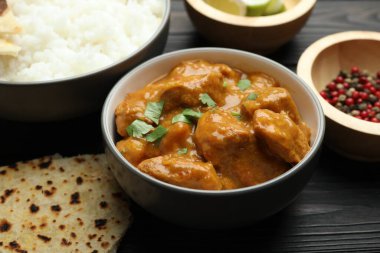 Delicious chicken tikka masala, rice, cilantro, lavash and spices on wooden table, closeup