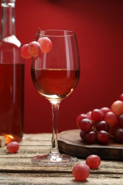 Cam, şişe ve üzümlü gül şarabı ahşap masada kırmızı arka planda, yakın planda.