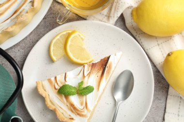Slice of tasty lemon meringue tart with mint served on light grey table, flat lay