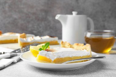 Slice of tasty lemon meringue tart with mint served on light grey table, closeup