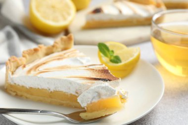 Slice of tasty lemon meringue tart with mint served on light grey table, closeup