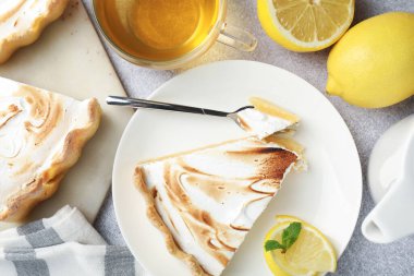 Slice of tasty lemon meringue tart with mint served on light grey table, flat lay