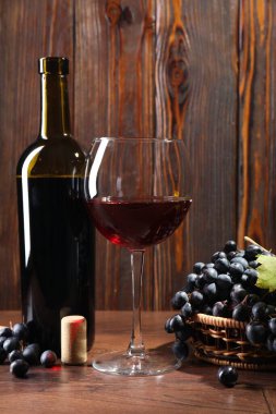 Red wine in glass, bottle, cork and grapes on wooden table, closeup
