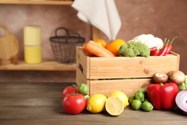 Different fresh raw vegetables and fruits in crate on wooden table indoors, closeup. Space for text