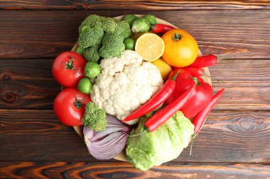 Different fresh raw vegetables and fruits in bowl on wooden table, top view