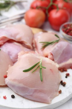 Raw chicken thighs with rosemary, peppercorns and tomatoes on white table, closeup