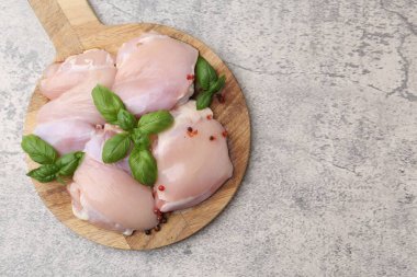 Raw chicken thighs with basil and peppercorns on light table, top view. Space for text