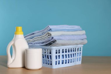 Açık mavi arkaplan, temiz giysiler ve ahşap masa üzerinde deterjan dolu çamaşır sepeti, metin için yer