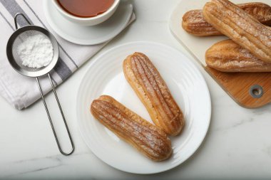 Delicious eclairs served on white table, flat lay