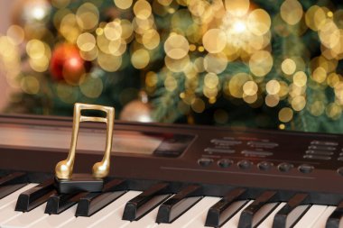 Kapalı alandaki Noel ağacının yanındaki piyanoda altın müzik notası.