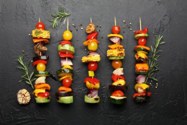 Skewers with tasty grilled vegetables on black table, flat lay
